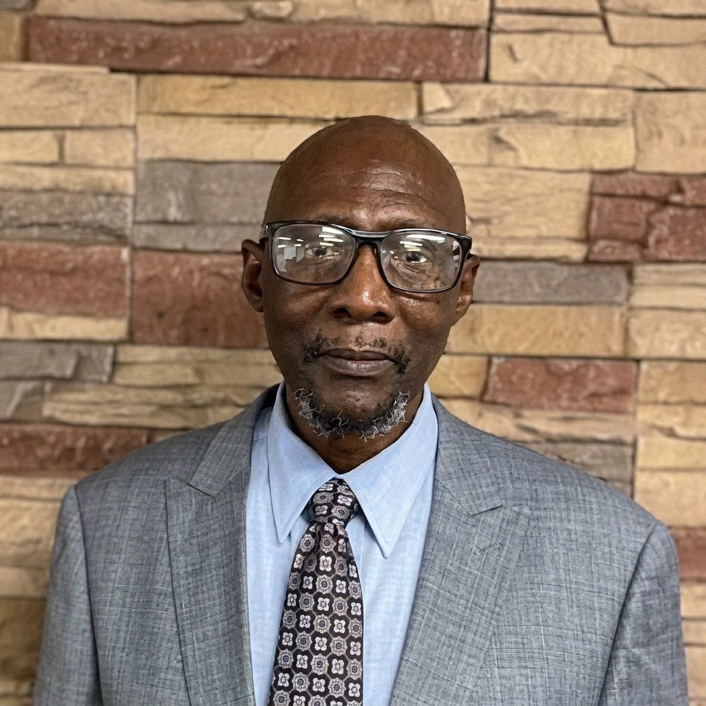 Man in gray suit and glasses before stone wall